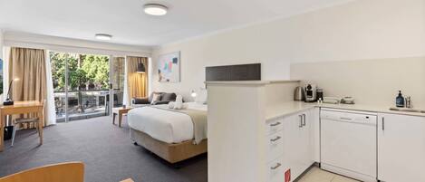 A hotel room with a bed, a desk, a dining table, a kitchenette, and a balcony with a view.