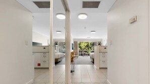 A hotel corridor with a mirrored wall, two beds, a small table, and a chair. - Marvelous Manly with Gym and Sauna (Manly)