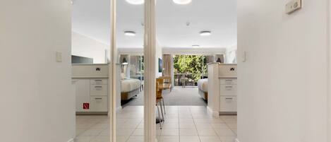 A hotel corridor with a mirrored wall, two beds, a small table, and a chair.