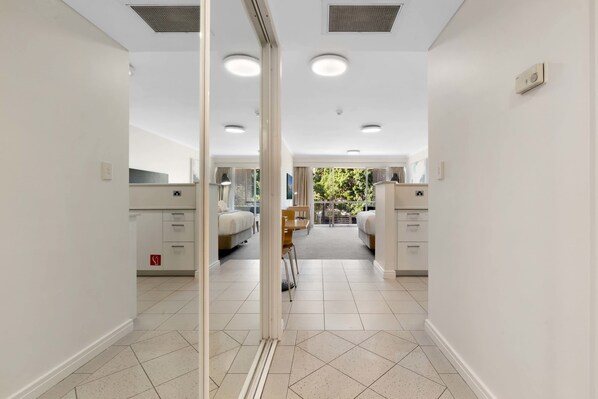 A hotel corridor with a mirrored wall, two beds, a small table, and a chair.