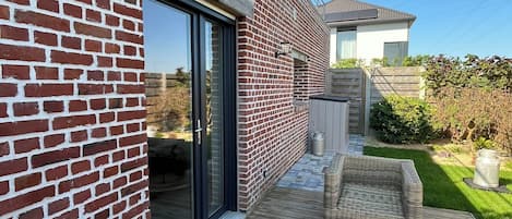 Una casa moderna con fachada de ladrillo, terraza de madera y mobiliario de mimbre para exteriores.