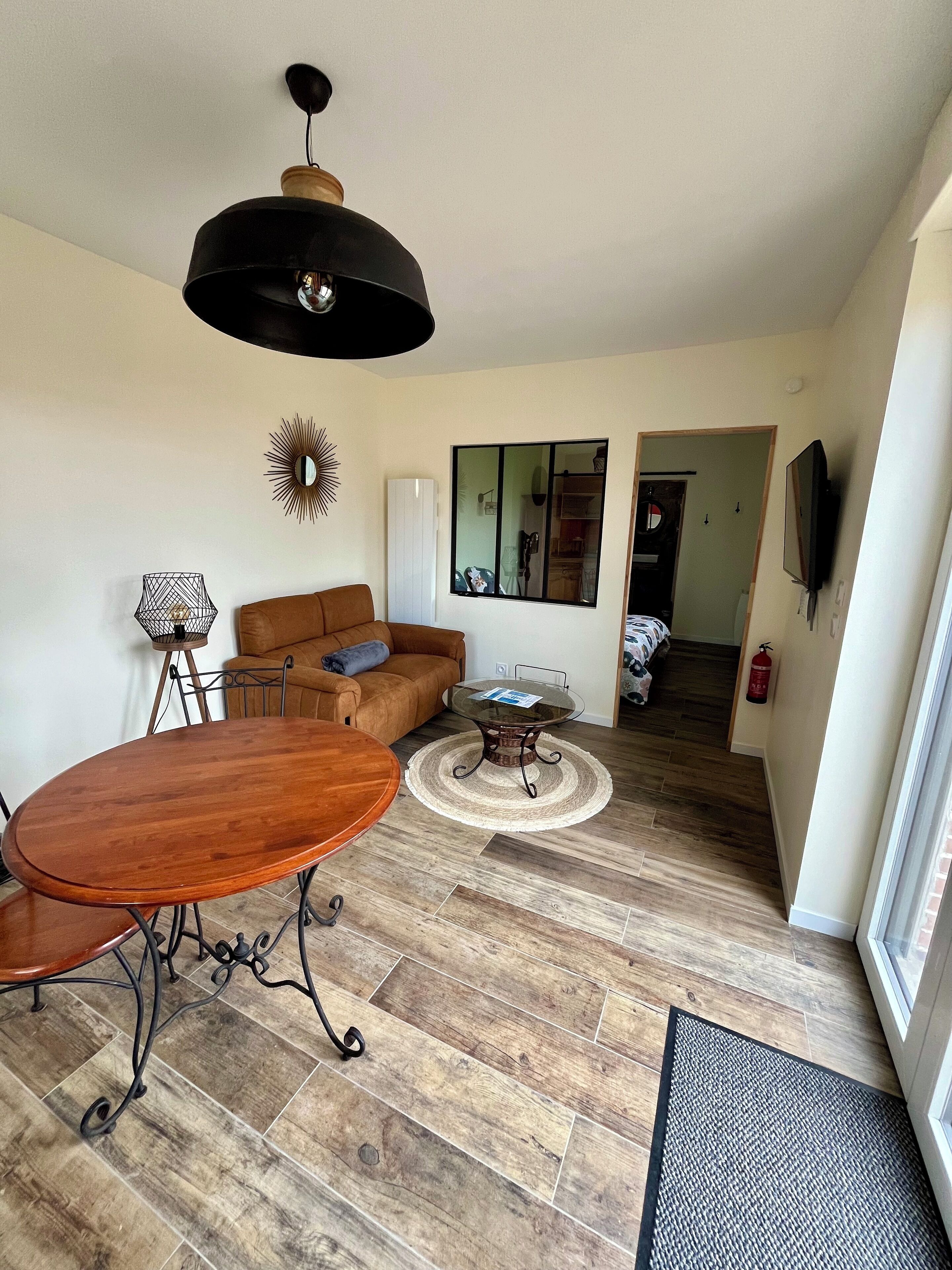 Un salon spacieux avec une table à manger en bois, un canapé marron, une table basse en verre et une suspension noire.