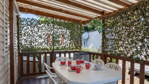 Une terrasse couverte, dotée d’une table et de chaises, entourée d’une clôture en bois et de plantes grimpantes.