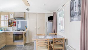 Une cuisine compacte équipée d’une cuisinière à gaz, d’un four et d’un réfrigérateur. On y trouve une table à manger avec quatre chaises et une fenêtre avec des rideaux.