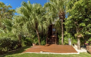 A wooden deck leading to a staircase surrounded by lush greenery and palm trees. - Northlight by BSL Rentals (Paynes Bay)