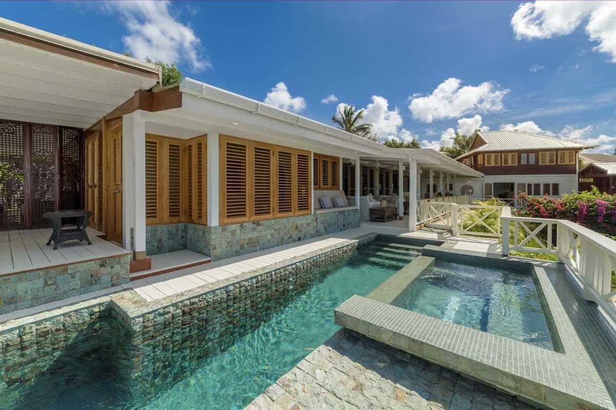 A pool area with a covered patio, wooden shutters, and a white fence.