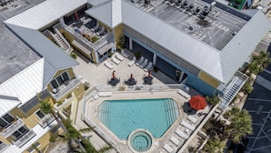 An aerial view of a hotel with a central swimming pool, outdoor seating, and palm trees.