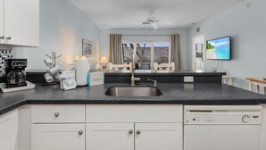 A modern kitchen with a black countertop, white cabinets, a built-in dishwasher, and a window with curtains.