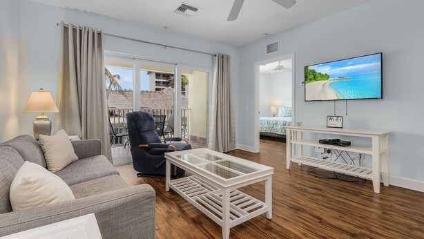 A modern living room with a sofa, armchair, glass coffee table, and a TV mounted on the wall.