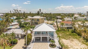 A coastal residential area with multiple houses, a prominent white house with a balcony, and palm trees. - Beach Time 146 Delmar Ave 3 Bedroom Home by RedAwning (Fort Myers Beach)