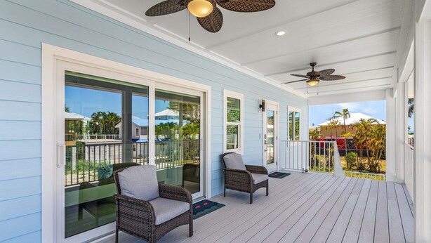 A covered porch with two wicker chairs, a ceiling fan, and a view of the surrounding area. - Beach Time 146 Delmar Ave 3 Bedroom Home by RedAwning (Fort Myers Beach)