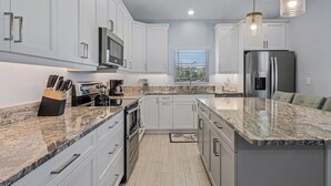 A modern kitchen with white cabinets, granite countertops, stainless steel appliances, and pendant lighting. - Beach Time 146 Delmar Ave 3 Bedroom Home by RedAwning (Fort Myers Beach)