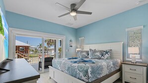 A bedroom with a bed, a ceiling fan, a nightstand, and a view of the outside. - Beach Time 146 Delmar Ave 3 Bedroom Home by RedAwning (Fort Myers Beach)