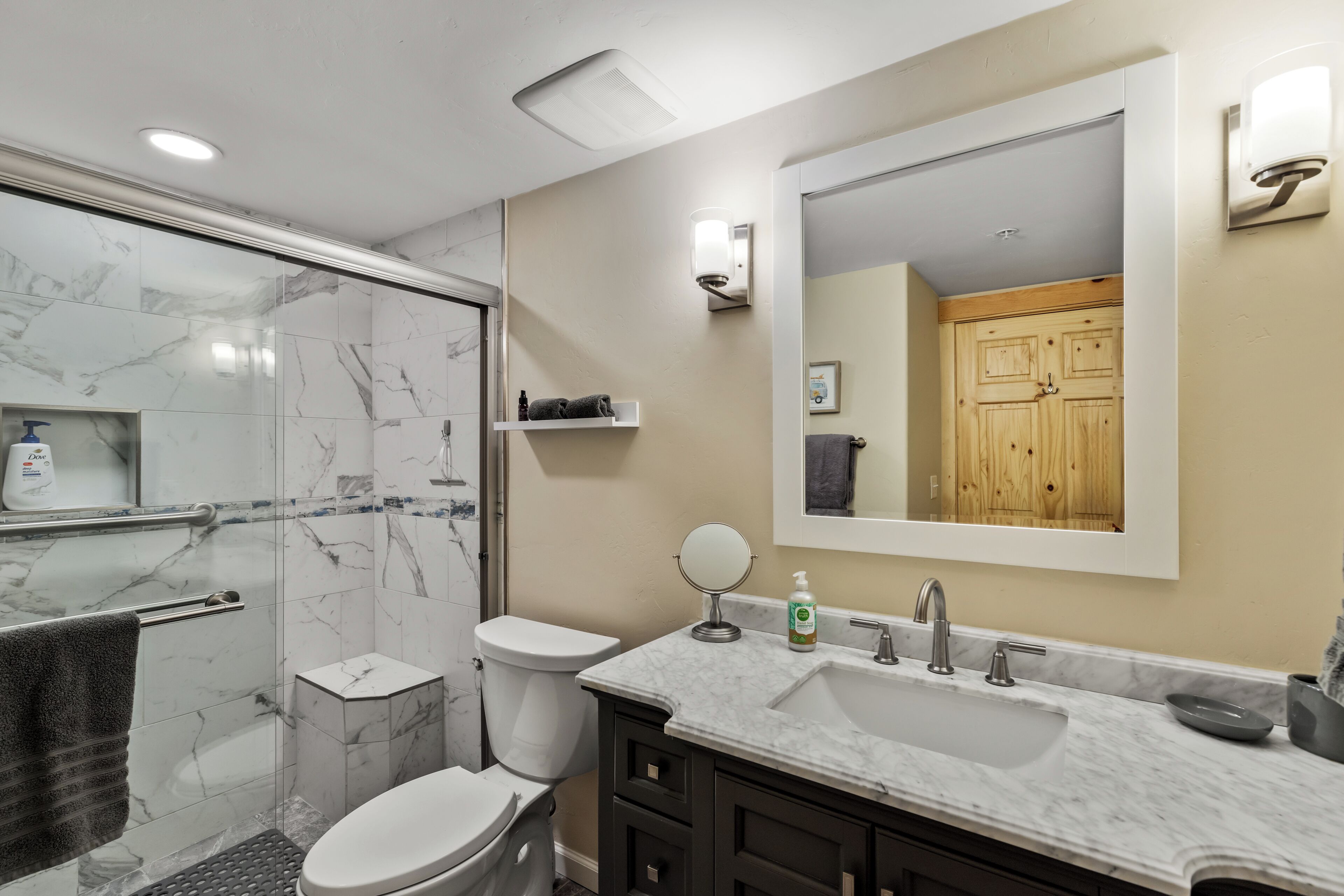 A modern bathroom with a glass shower enclosure, a toilet, a sink with a vanity, and a mirror.