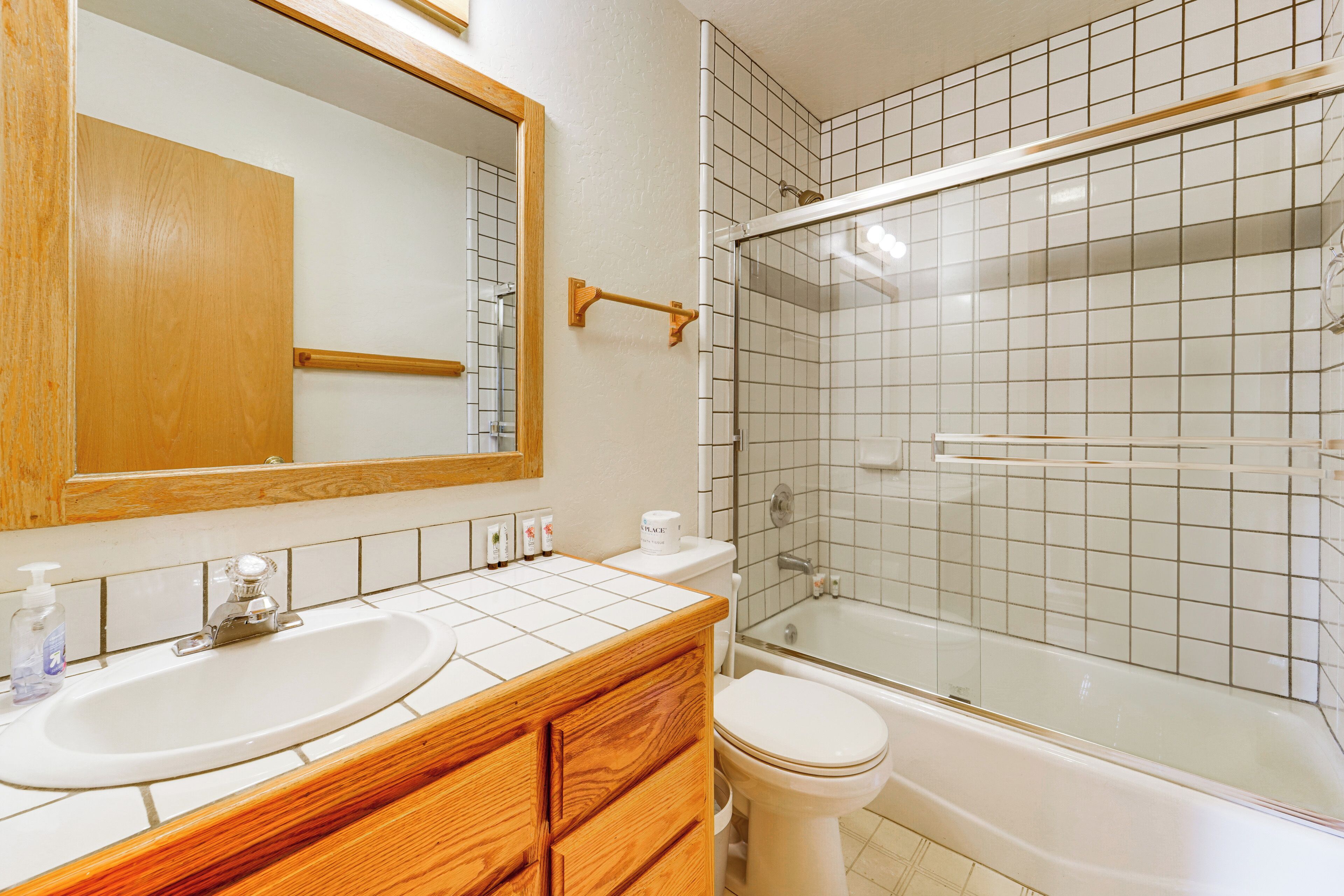 Ein Badezimmer mit einem Holzlagerfläschchen, einem Waschbecken, einem Spiegel, einer Toilette und einer Duschkabine.