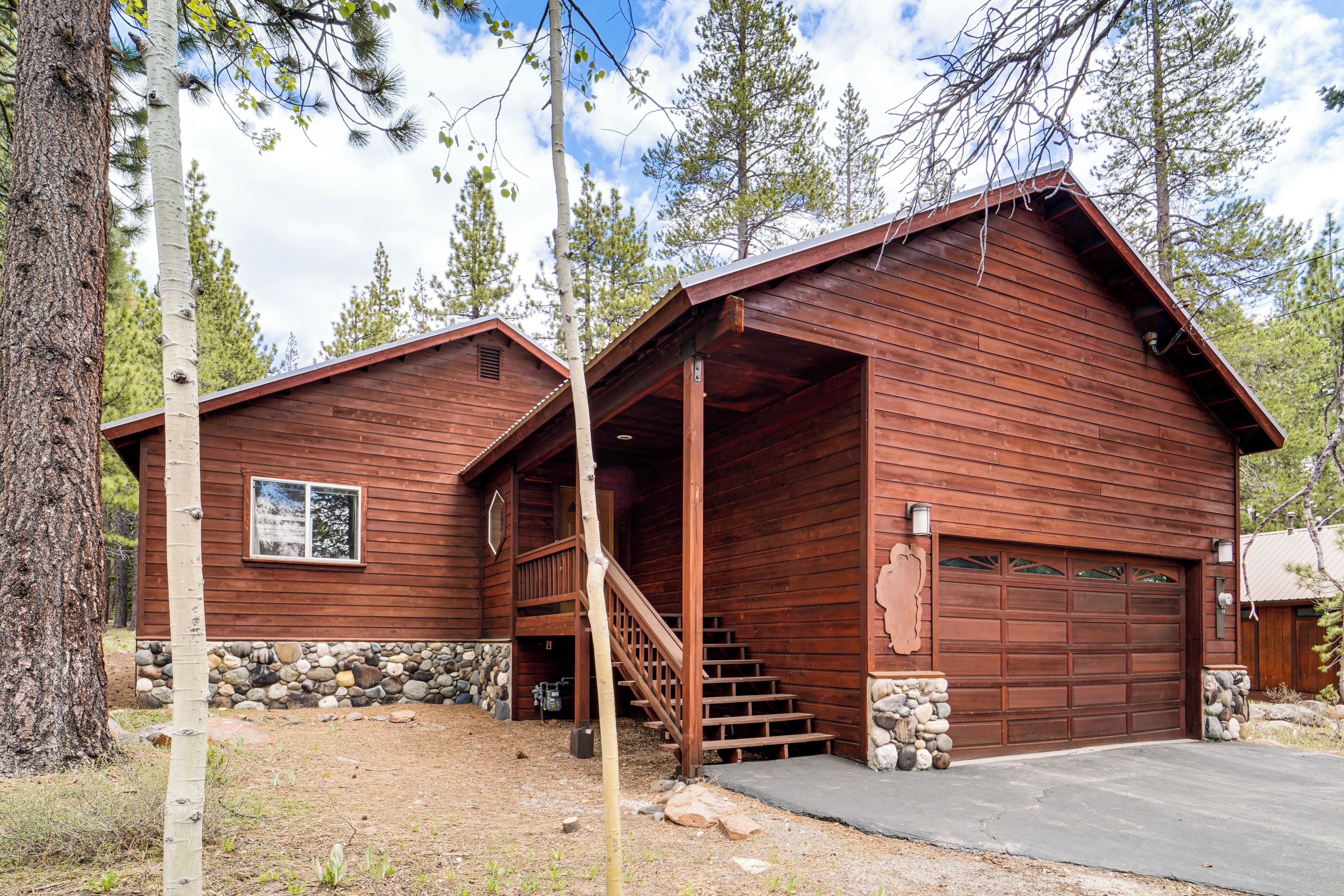 A wooden cabin with a stone foundation, a front porch, and a garage.