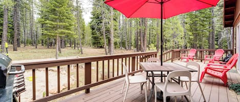A wooden deck with a table and chairs, surrounded by a forest.