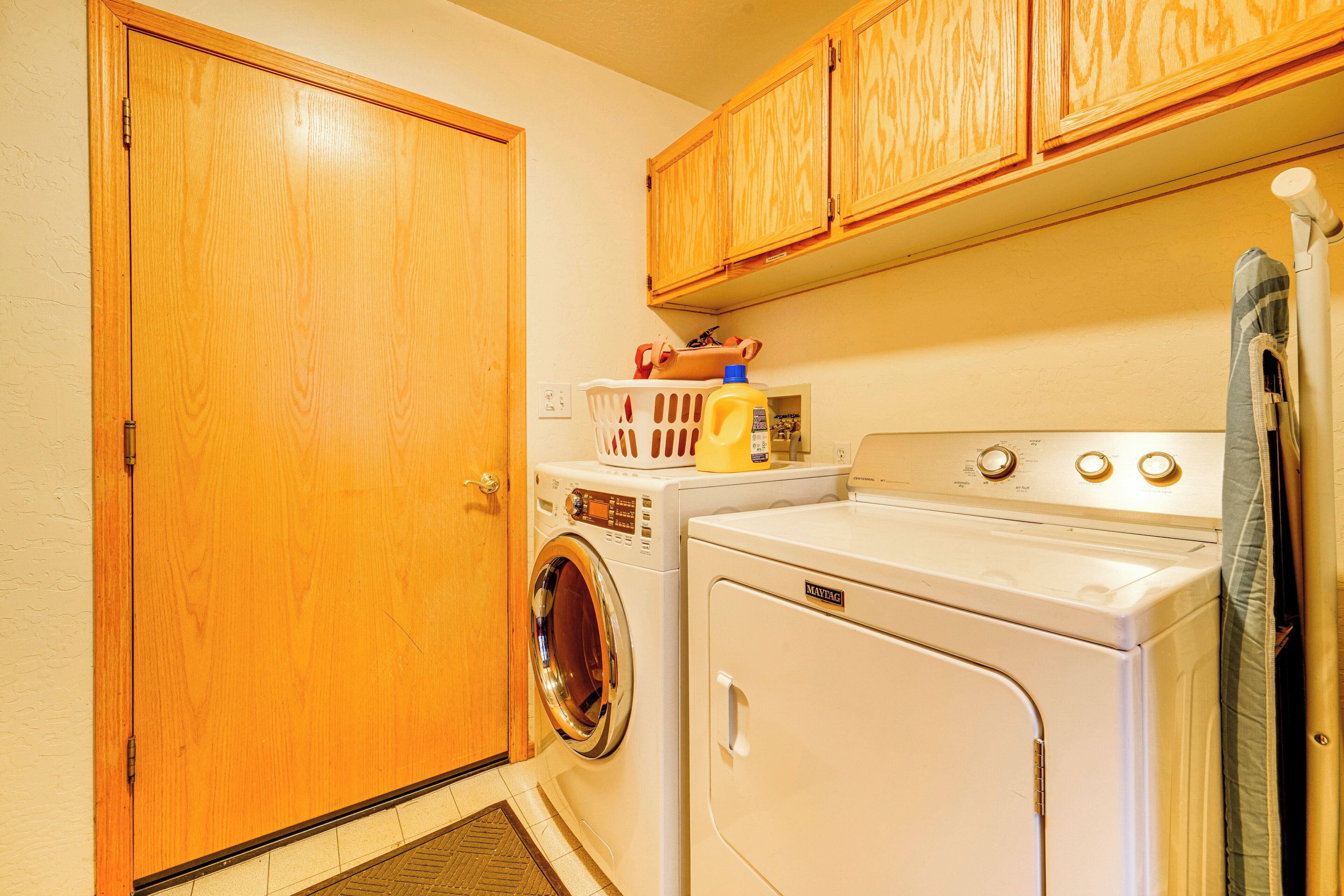 A laundry area with a front-loading washer and dryer, wooden cabinets above, and a door to the left.