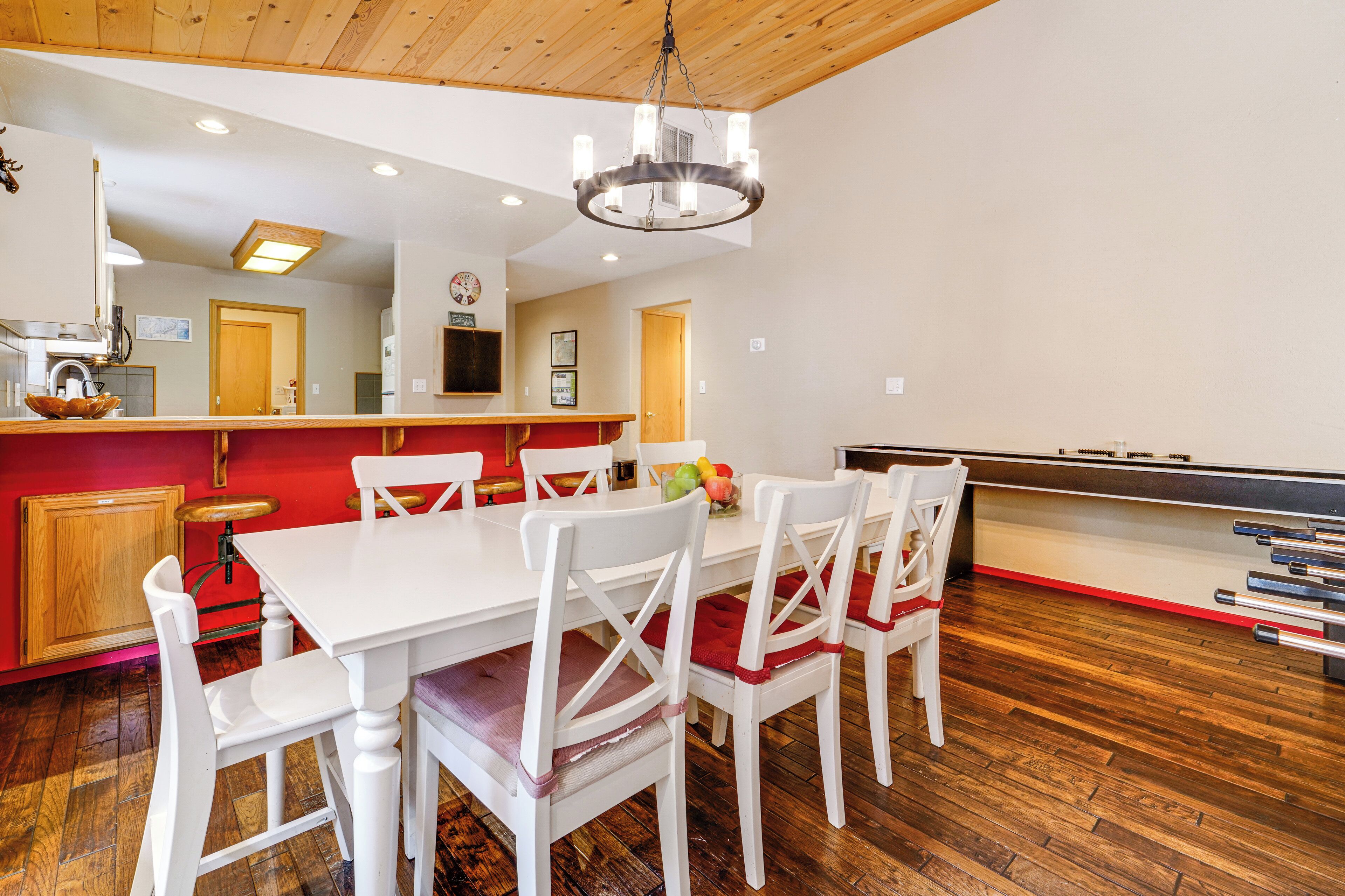 Un coin repas avec une table et des chaises blanches, un mur d’accent rouge et un plafond en bois.