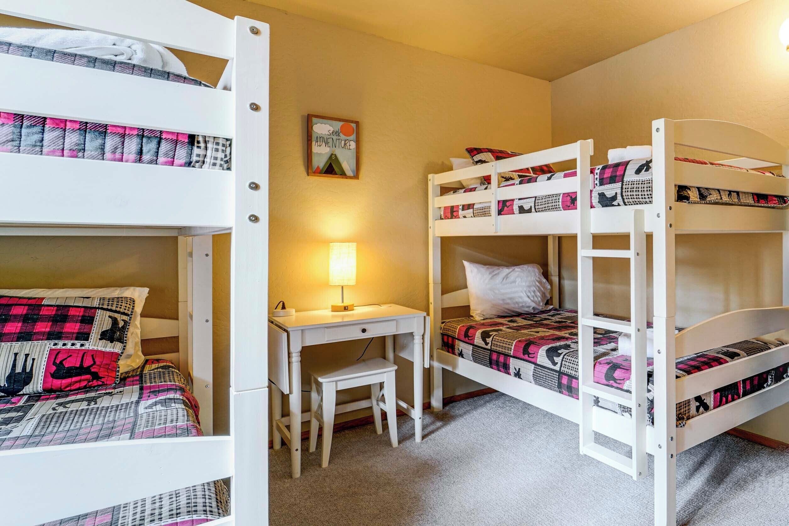 A bunk bed room with a desk and chair, a lamp, and a motivational poster on the wall.