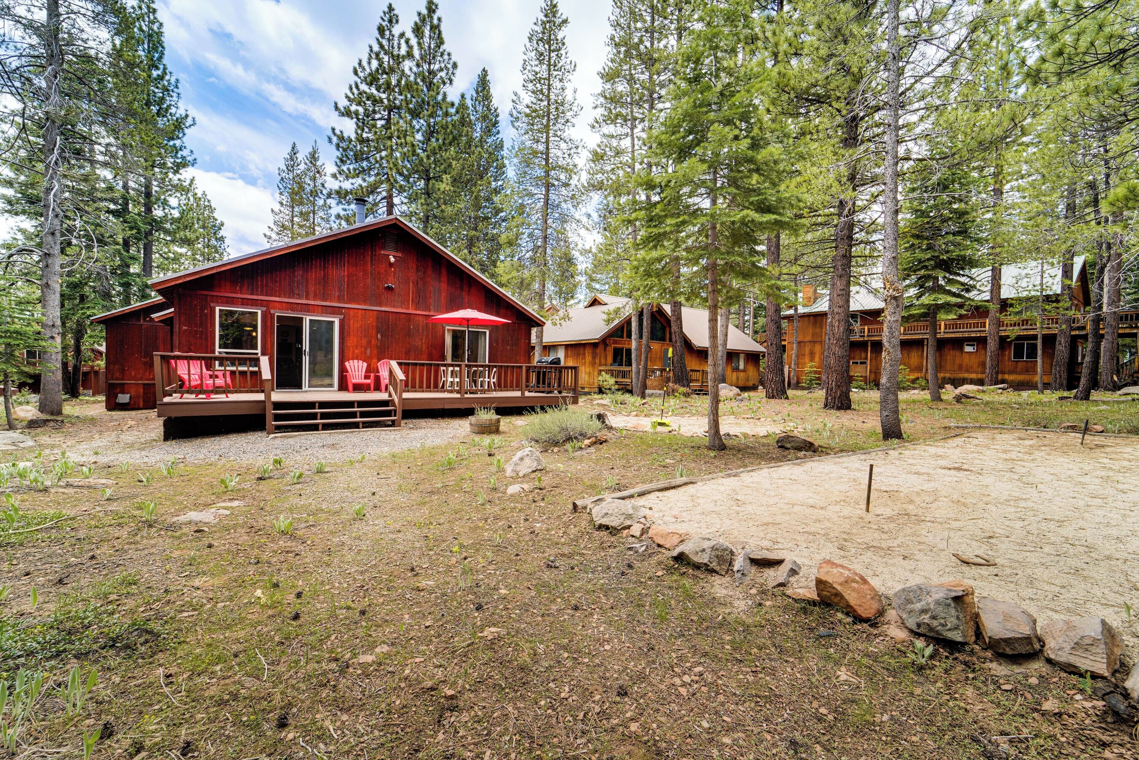 A rustic cabin with a red exterior, wooden deck, and a covered outdoor seating area.