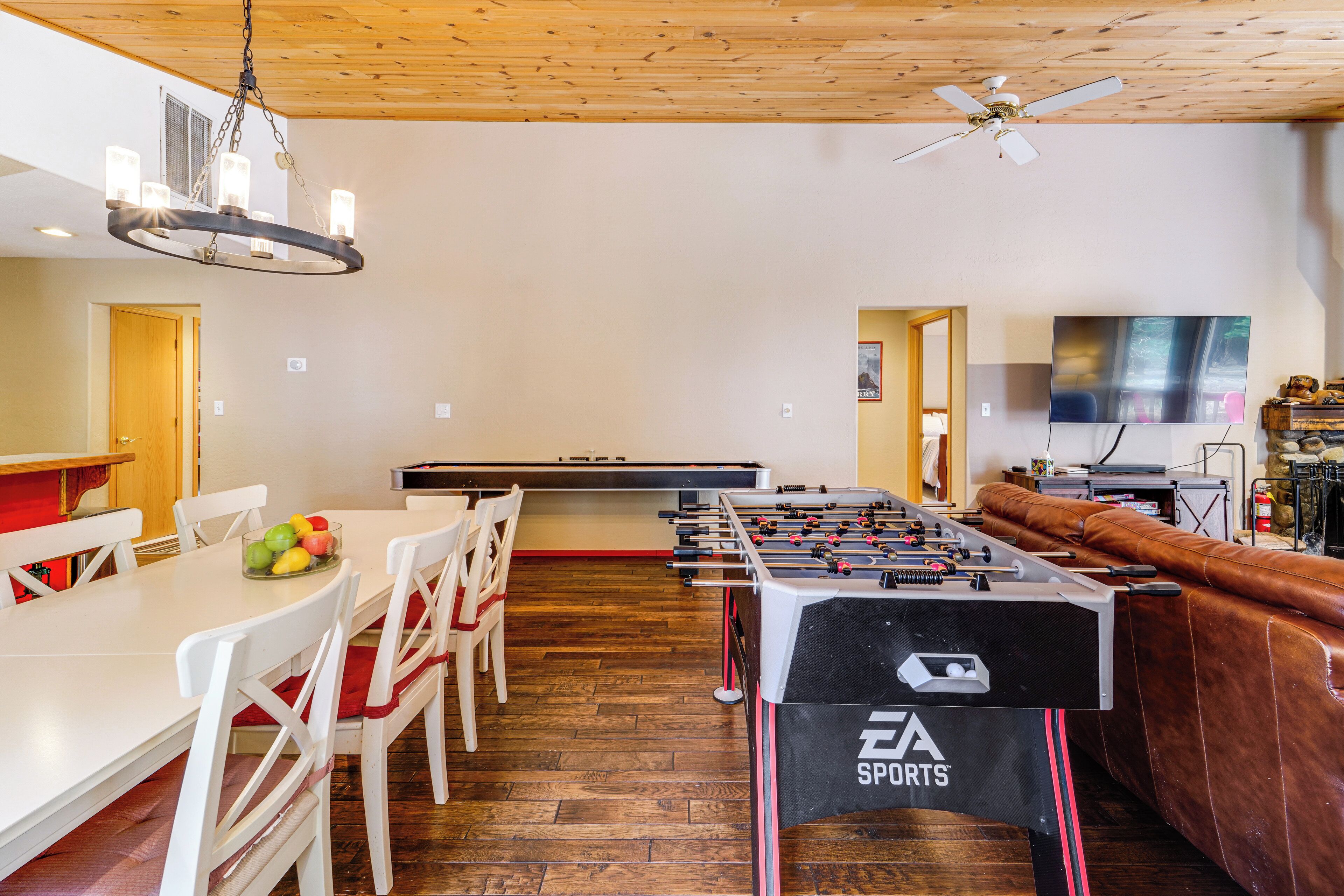 A spacious room with a foosball table, a billiards table, and a television mounted on the wall.