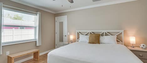 A bedroom with a bed, bedside lamps, a ceiling fan, a bench, and a window with blinds.
