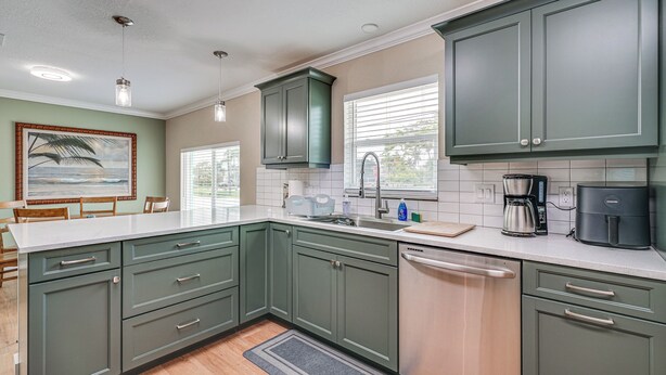 A kitchen with green cabinets, a dishwasher, a coffee maker, and a window with blinds.