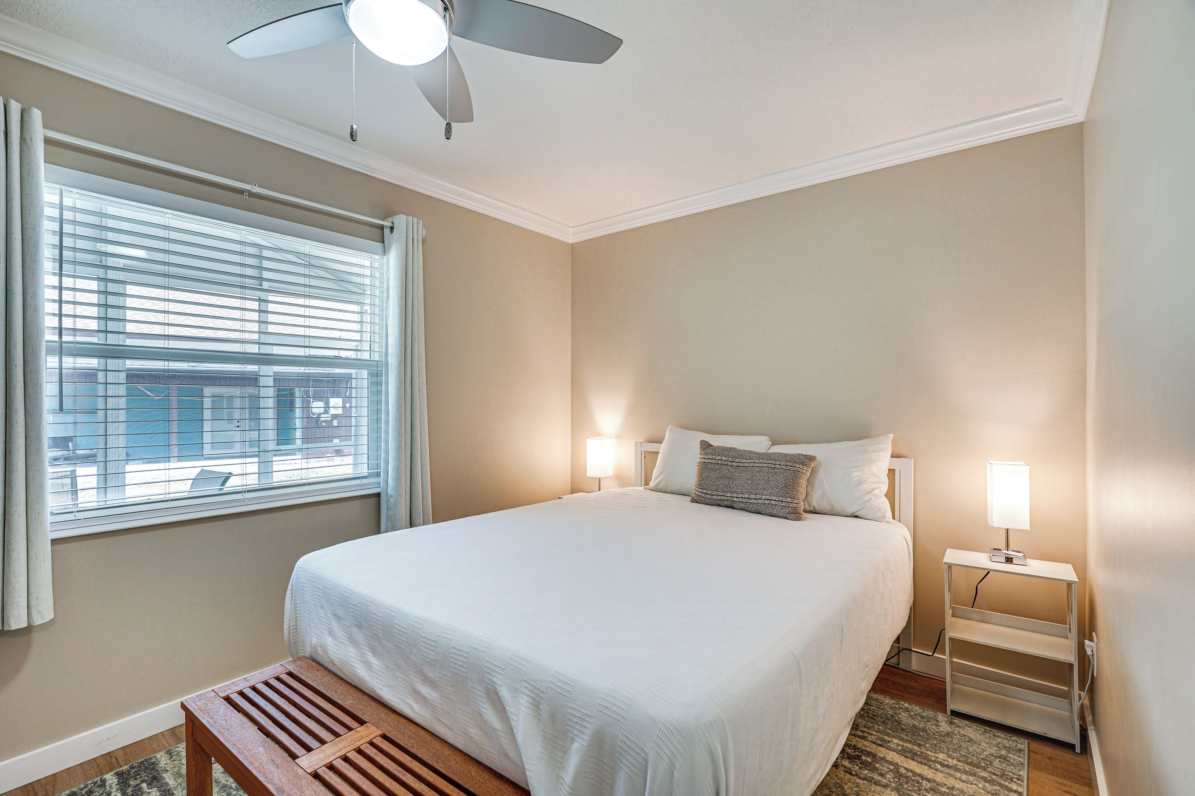Ein Schlafzimmer mit Bett, Nachttischen, Deckenventilator und Fenster mit Jalousien.