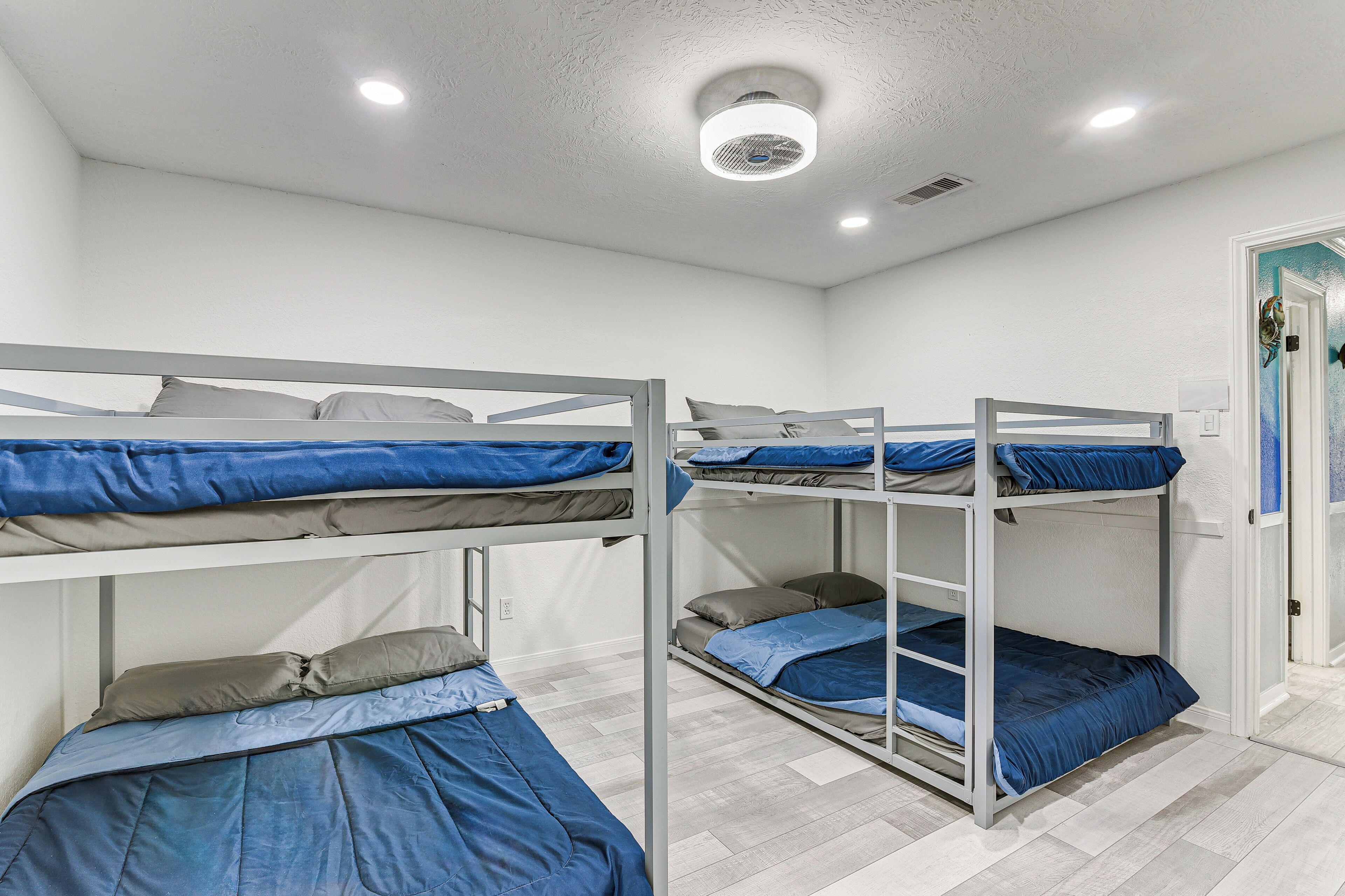 A dormitory room with bunk beds, white walls, and a ceiling light.