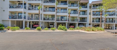 A multi-story hotel with balconies, a parking lot, and some landscaping.