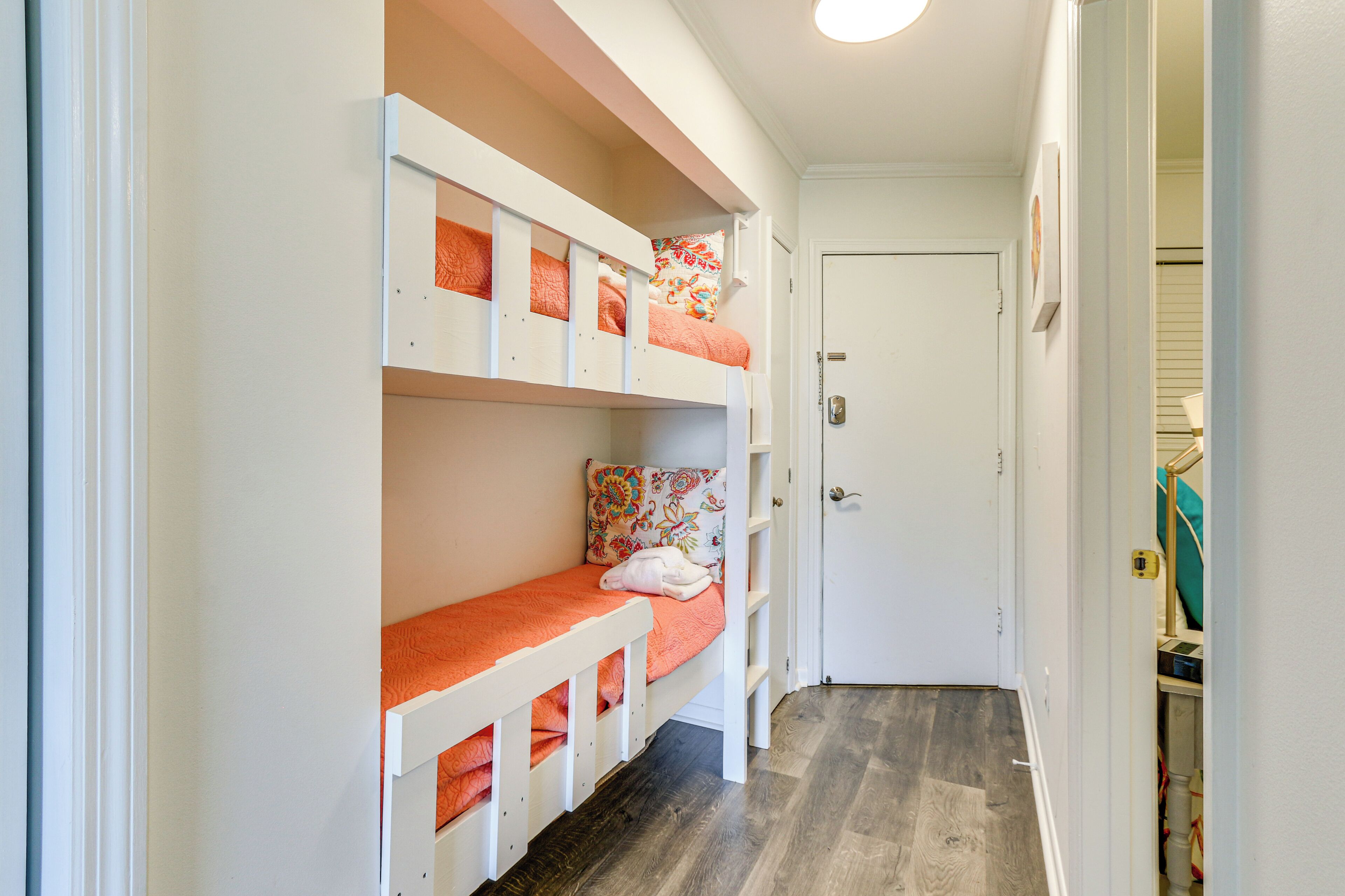 A narrow hallway with bunk beds, a white door, and a wooden floor.
