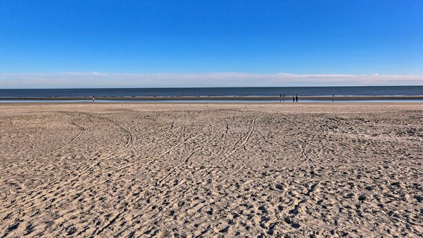 Een breed zandstrand met voetafdrukken die naar het water leiden.