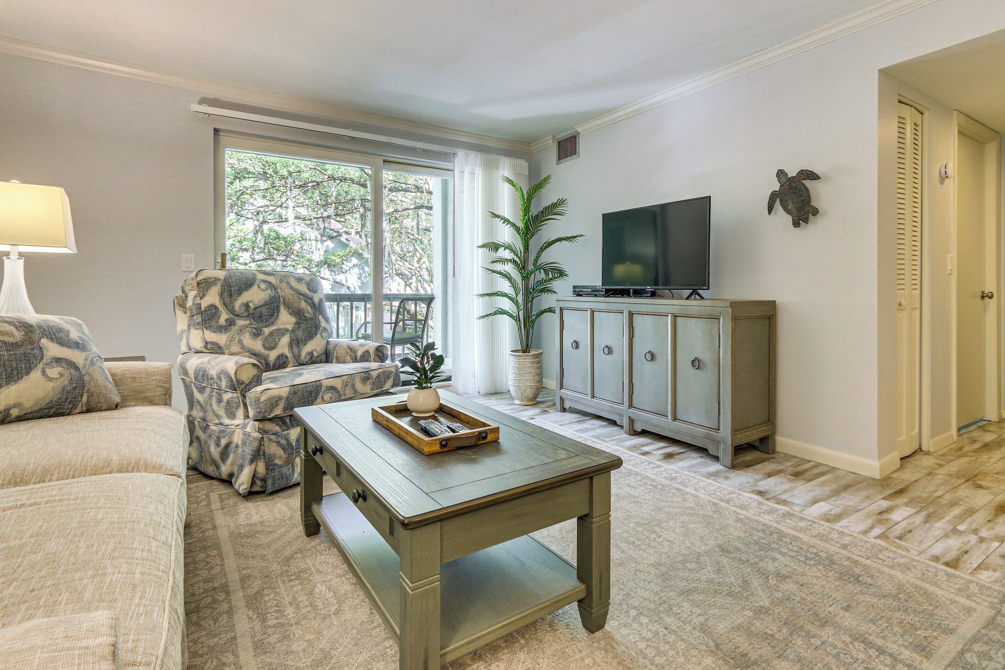 A living room with a sofa, armchair, coffee table, TV, and a potted plant.