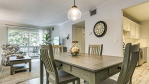 Un coin repas avec une table en bois, des chaises, un luminaire suspendu et une vue par la fenêtre.