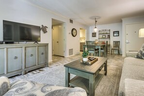 A living room with a television, a coffee table, and a sofa. There is a dining area with chairs and a table.