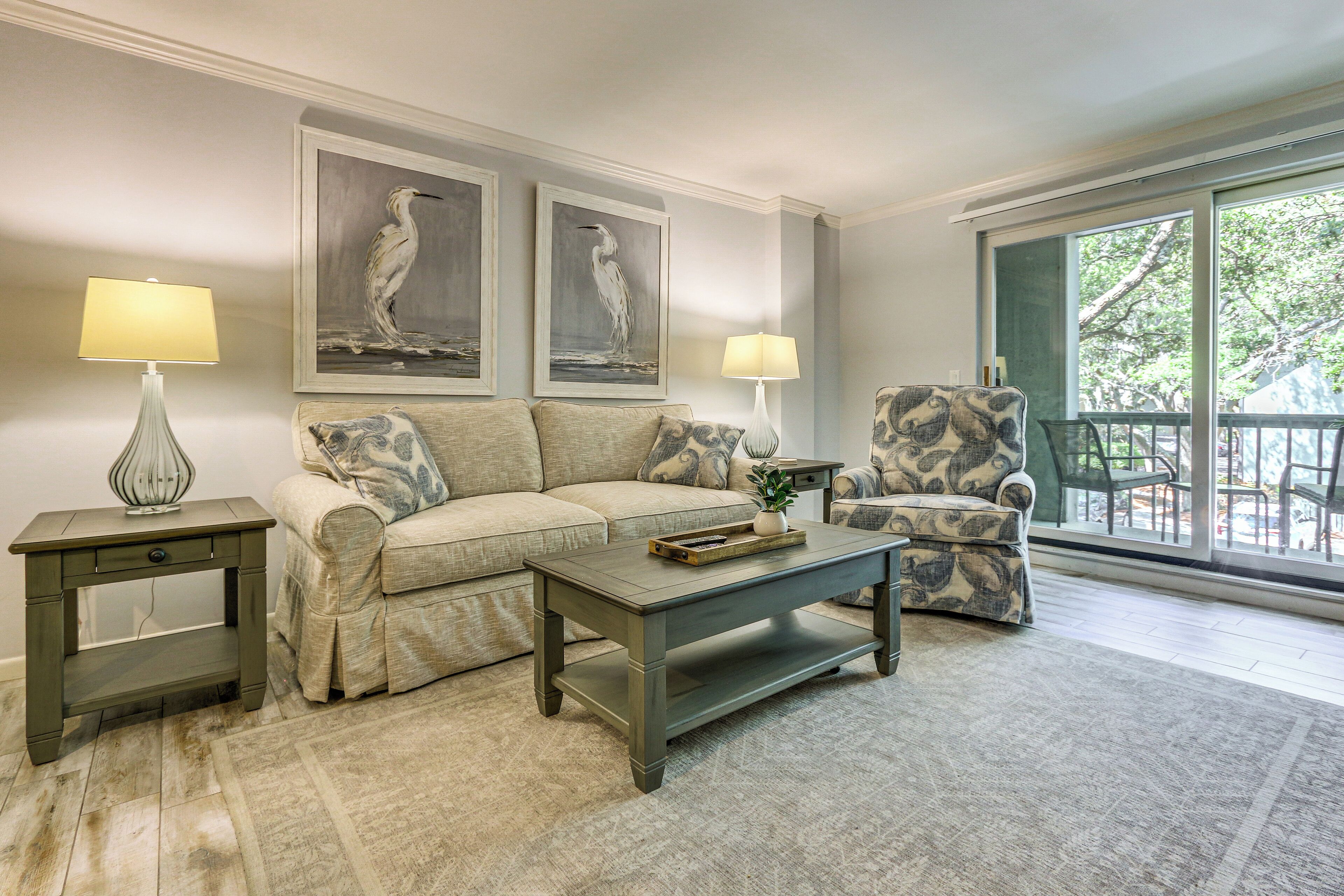 A living room with a sofa, armchair, coffee table, two lamps, and framed artwork on the wall.