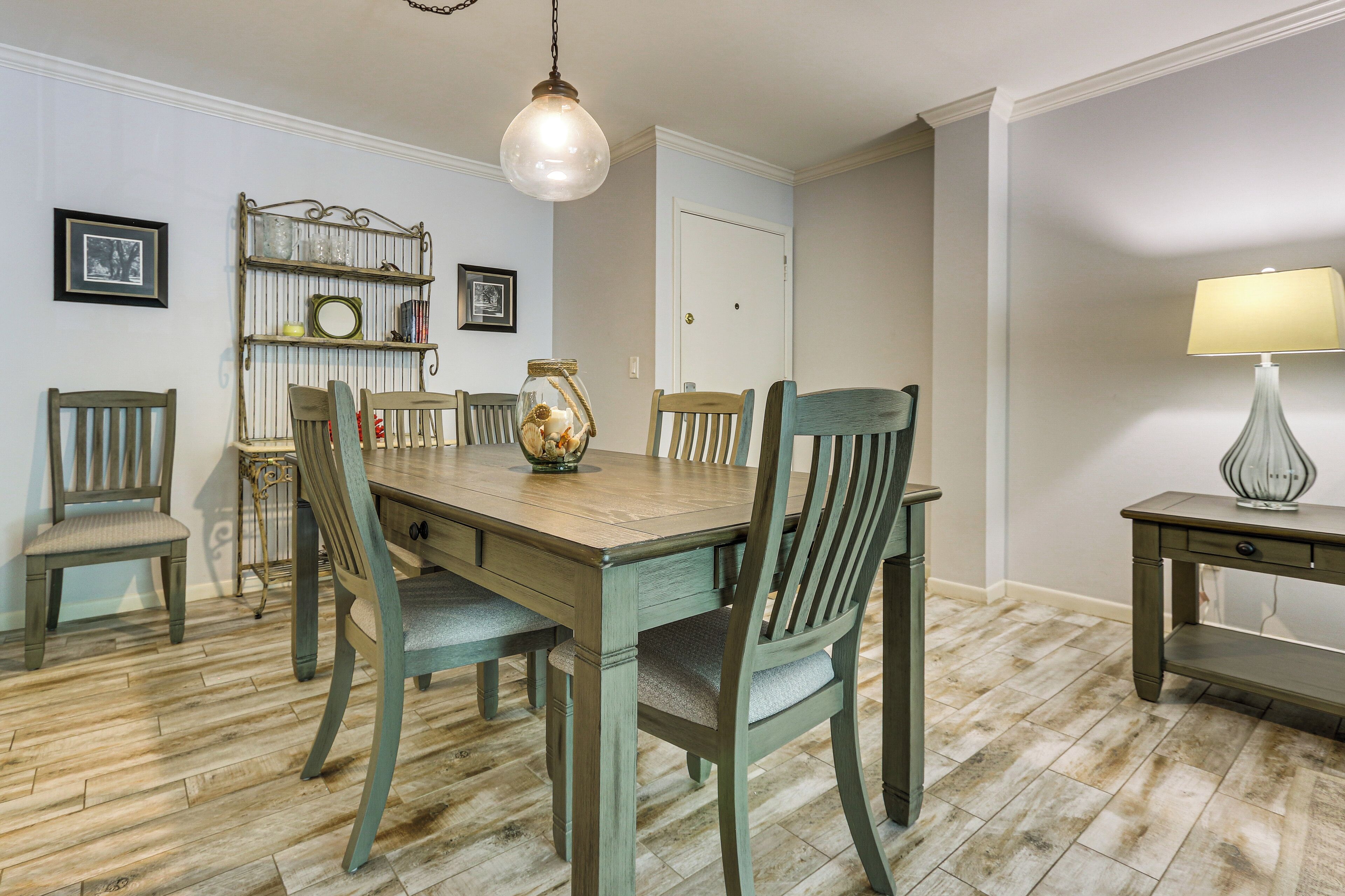 Un coin repas avec une table et des chaises en bois, un luminaire suspendu et une étagère fixée au mur, ornée d’objets décoratifs.