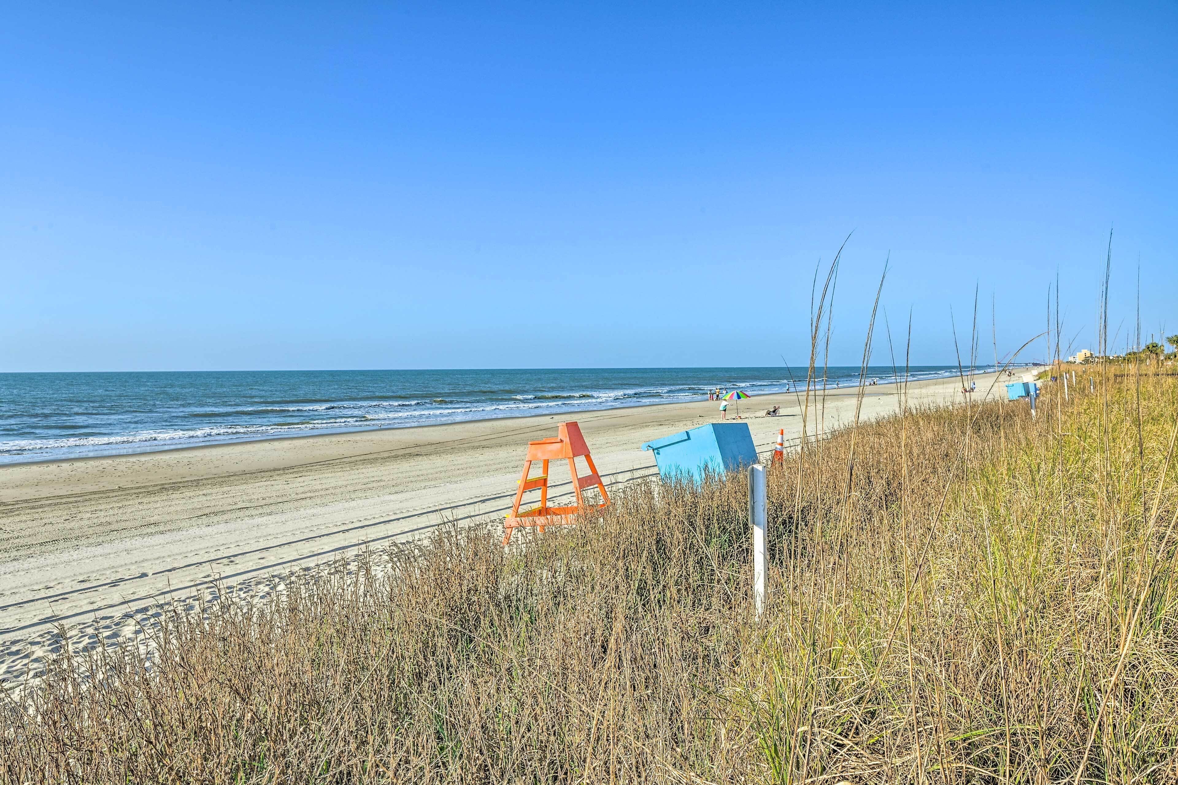 A beach with a sandy shore, a lifeguard tower, and tall grasses.