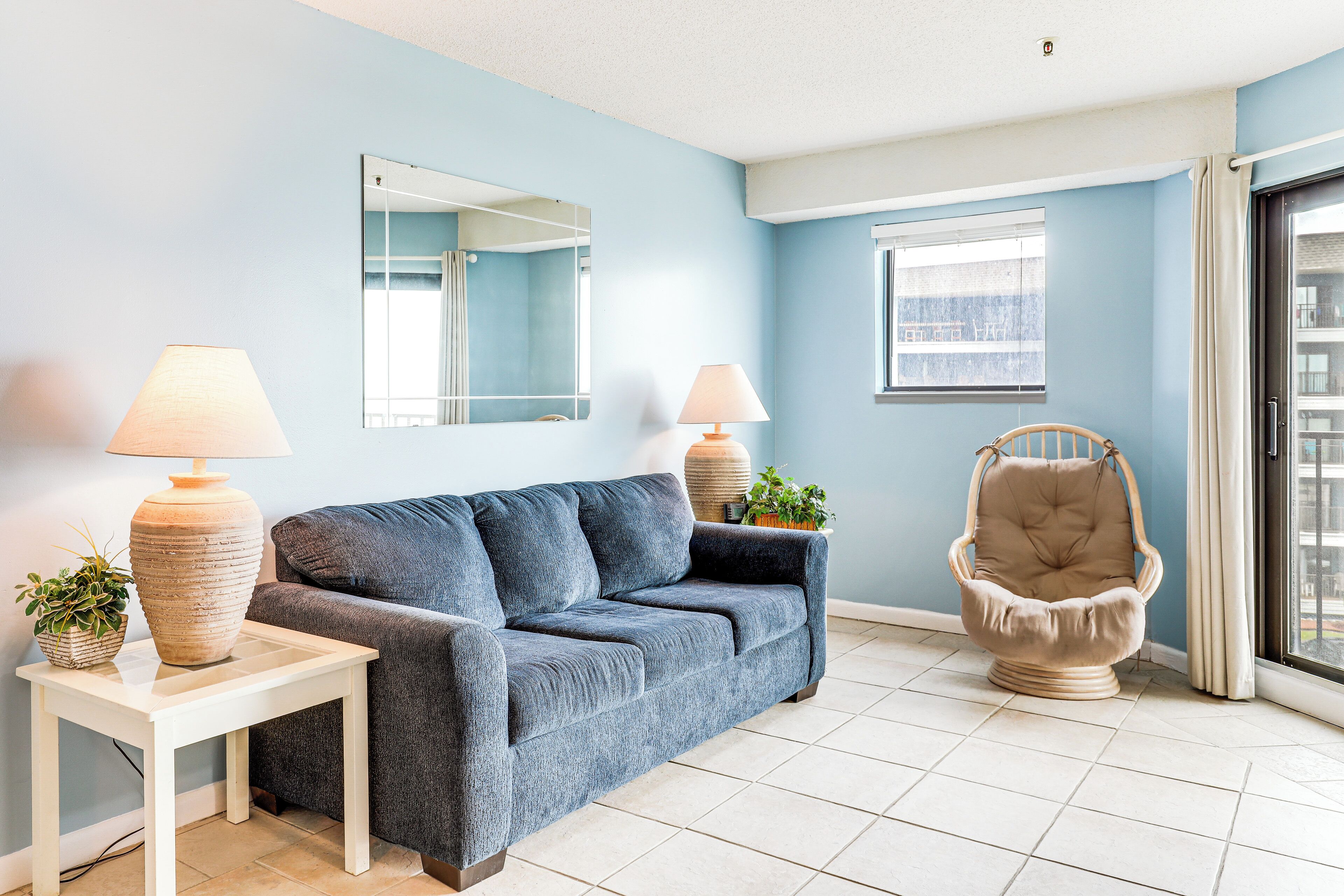 A living room with a sofa, two lamps, a chair, a small table, and a mirror.