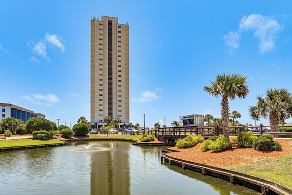 A tall building with a modern design, a calm water feature, and well-maintained landscaping.