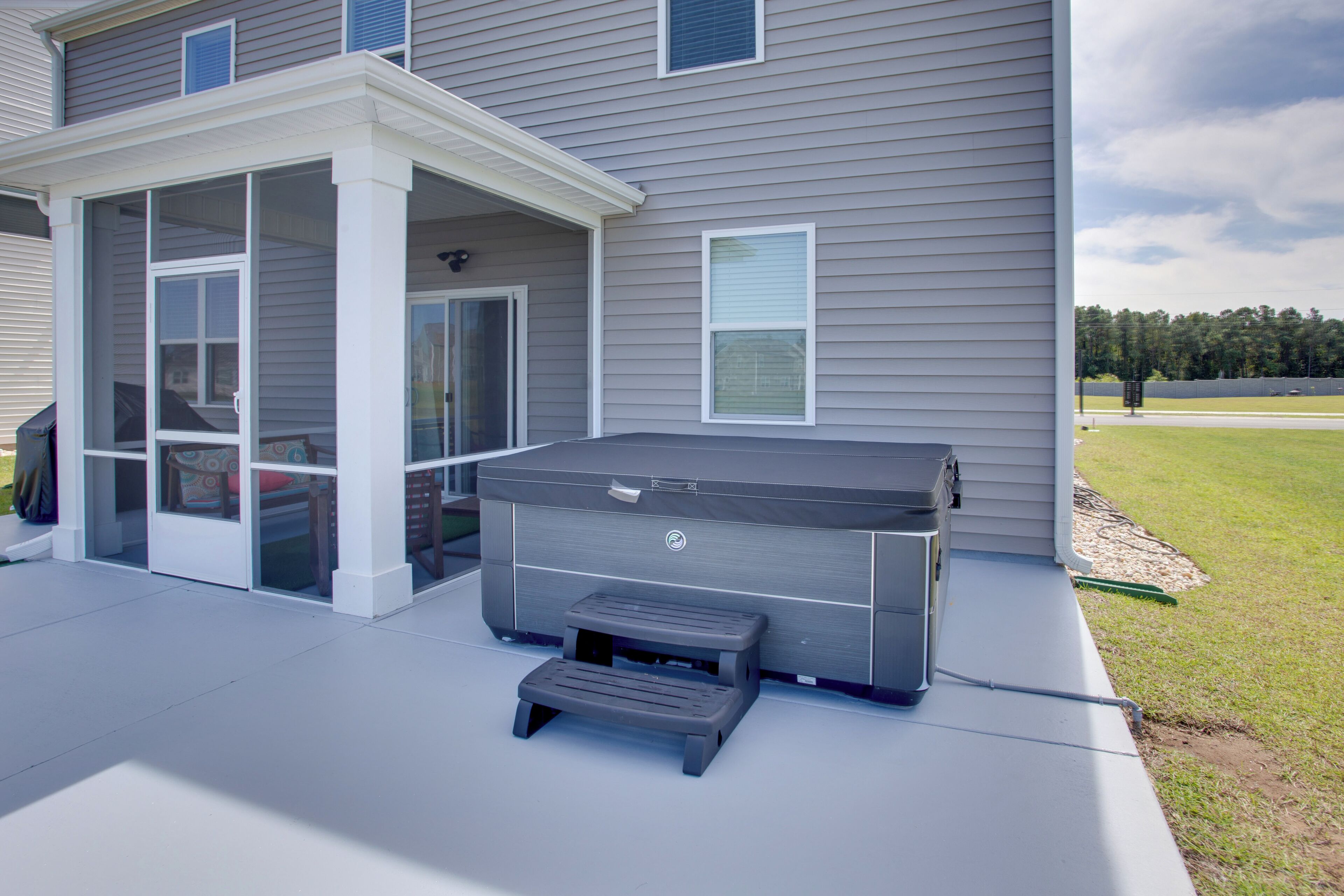 Eine überdachte Terrasse mit Whirlpool, einer kleinen Stufe und einem Grill.