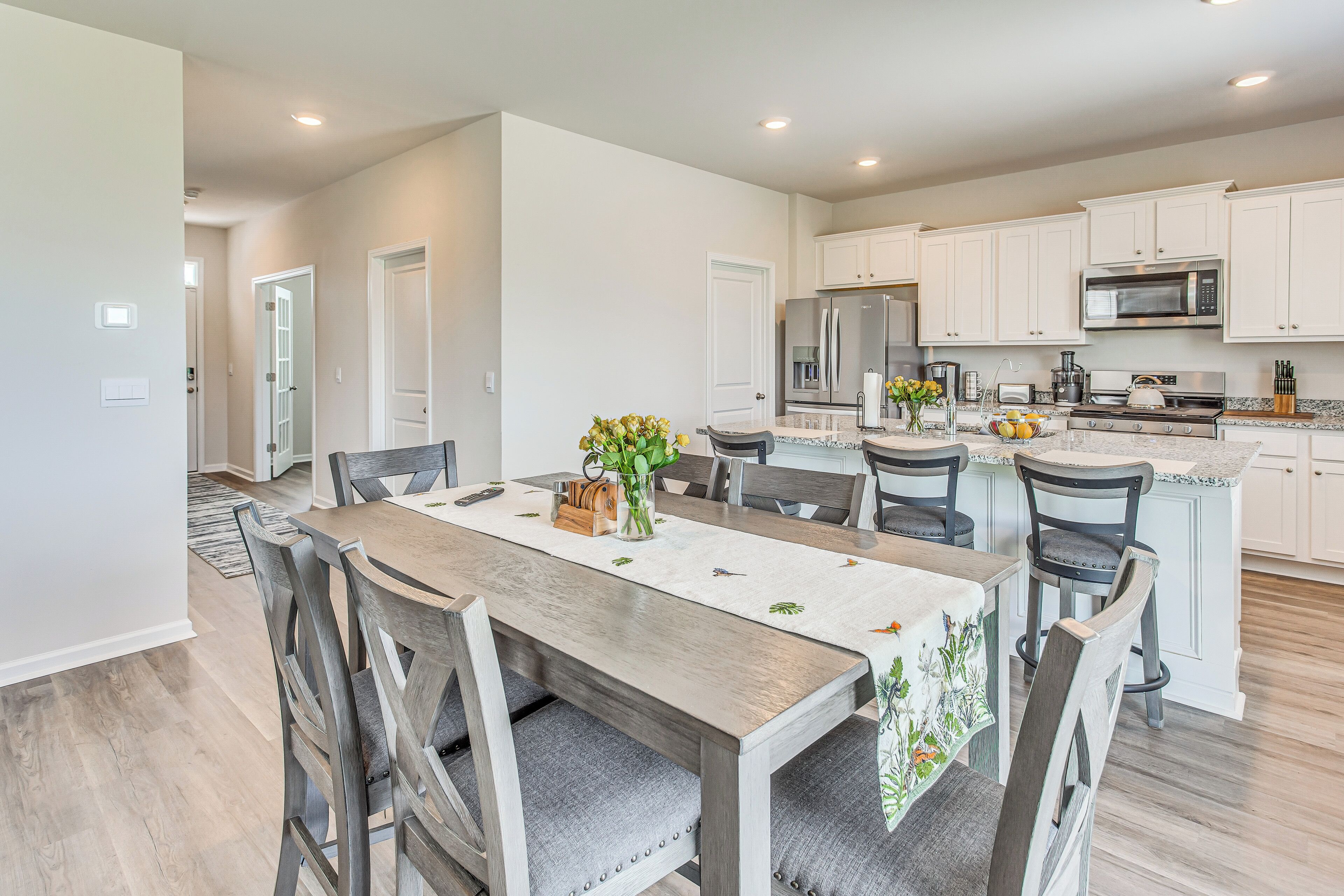 A modern kitchen with white cabinets, a wooden dining table, and a central island with a sink and stove.