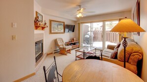 Una sala de estar con chimenea, ventilador de techo, sofá, mesa de centro y televisor.