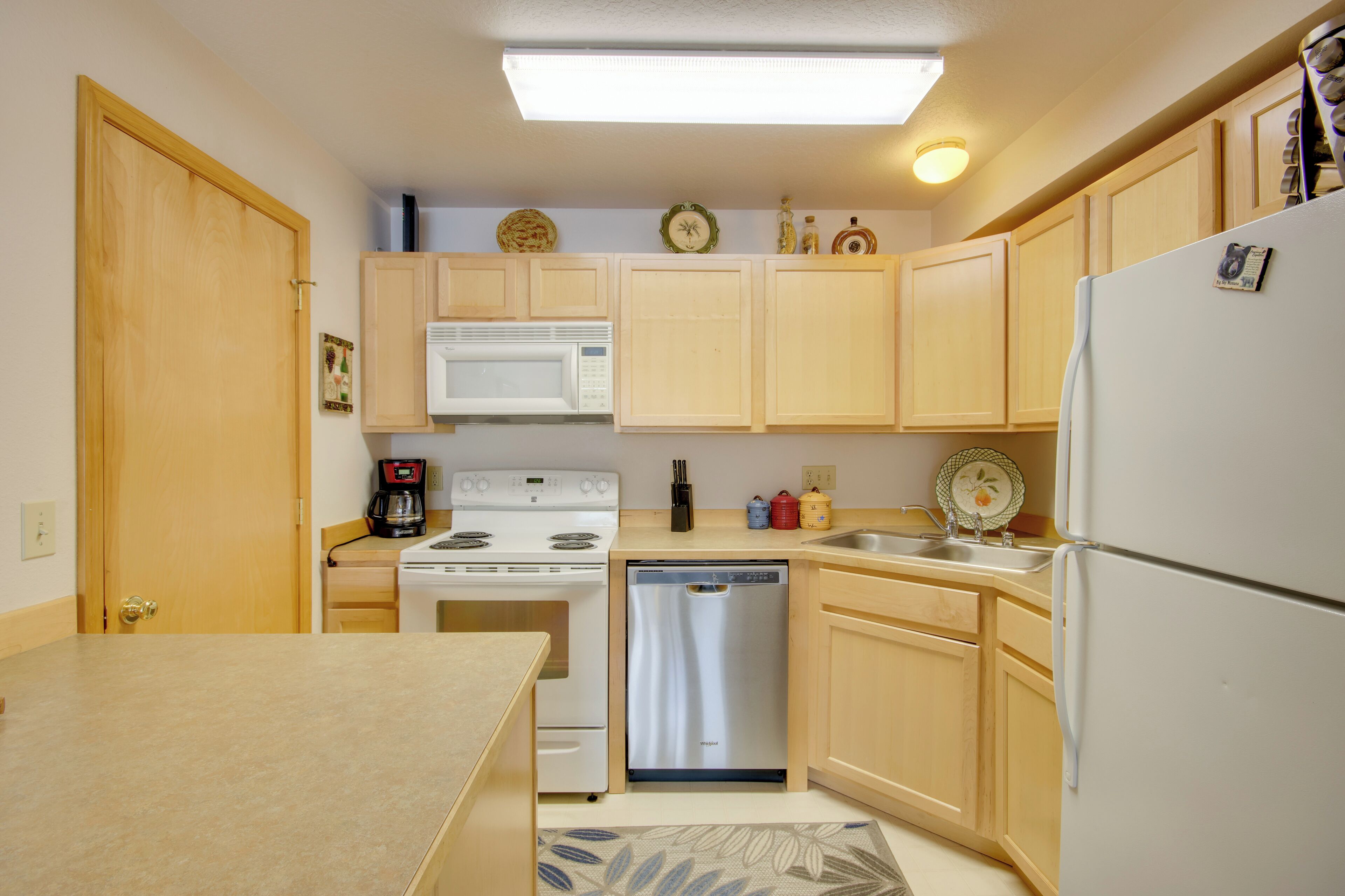 Una cocina compacta con armarios de madera, un refrigerador blanco, lavavajillas, estufa y microondas.