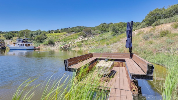 Un muelle de madera que se adentra en un río tranquilo, con una barca amarrada cerca y un cielo azul despejado.