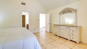 Quarto com uma cama grande, cômoda com espelho e porta que dá para outro espaço.