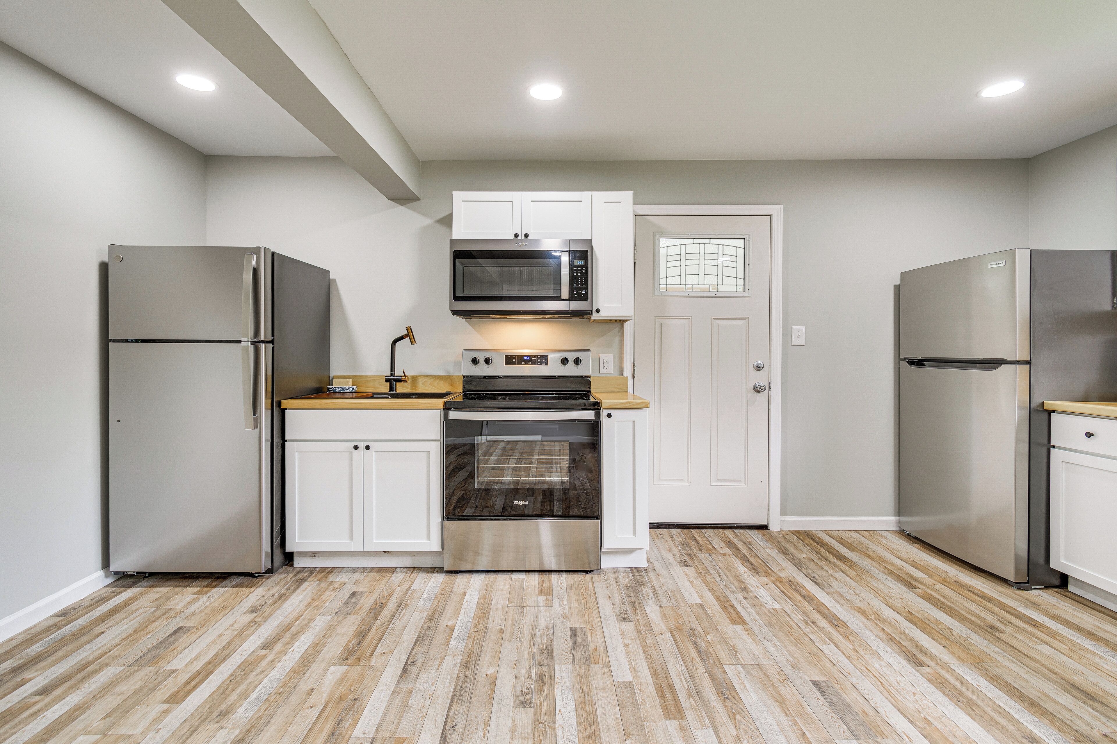 A compact kitchen with white cabinets, stainless steel appliances, and a wooden countertop.