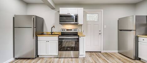 A compact kitchen with white cabinets, stainless steel appliances, and a wooden countertop.