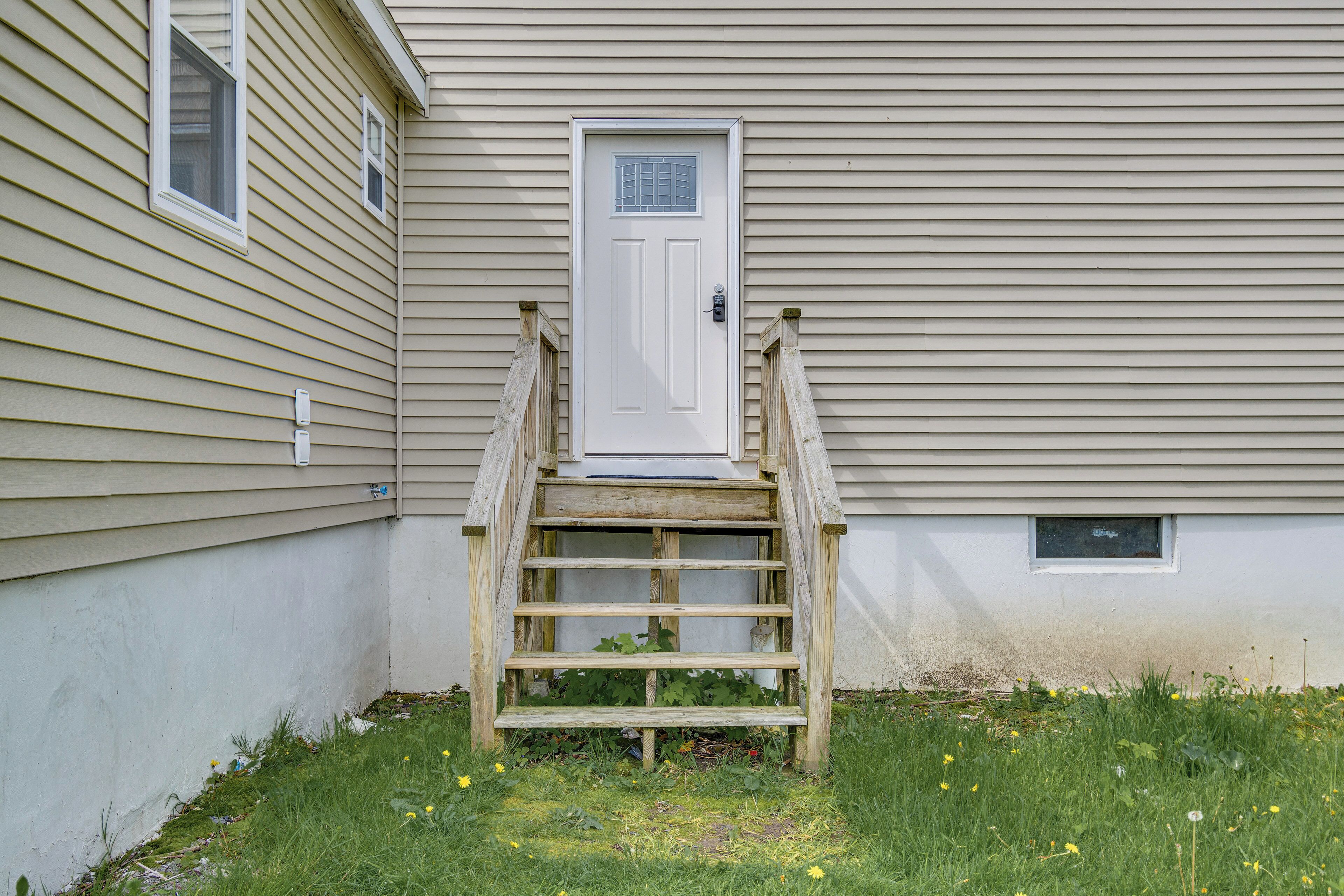 A wooden staircase leading to a white door with a small window above it, set against a beige building.